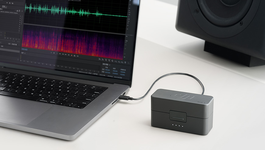 System mikrofonów bezprzewodowych DJI Mic 3 2 TX + 2 RX + Etui ładujące czarny grafika przedstawia etui ładujące leżące obok laptopa